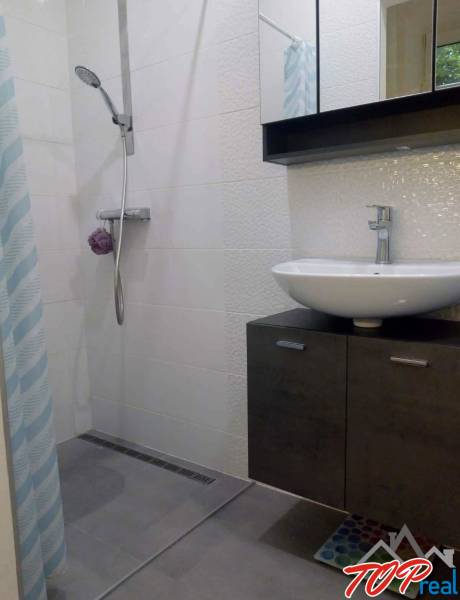 Fürdőszoba modern zuhanyzóval az egyszobás lakásban, világos csempék, mosdókagyló.