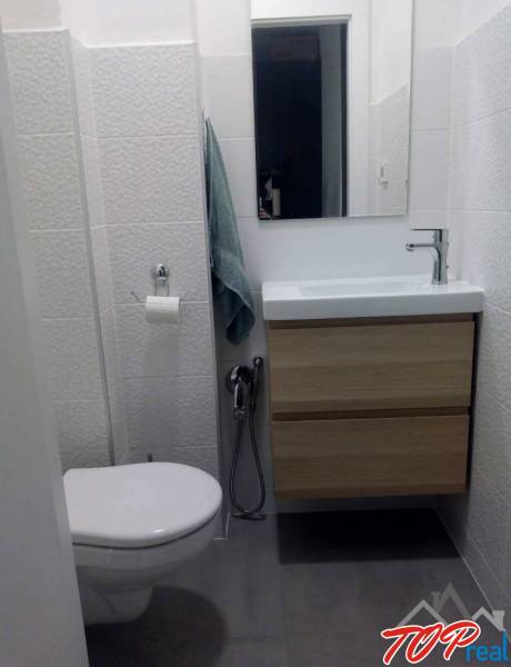 Kompakt fürdőszoba mosdóval és szekrénnyel egy egyszobás lakásban, finom textúrájú csempével.