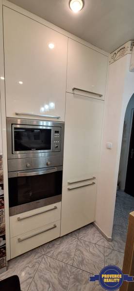 Konyha egy háromszobás lakásban fehér szekrényekkel és beépített készülékekkel.