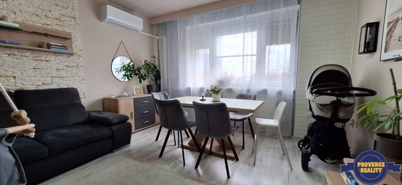 Nappali szürke kanapéval, fa dekorációs asztallal és finom függönyökkel egy háromszobás lakásban.