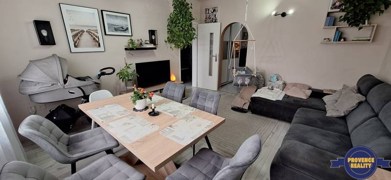 Nappali egy háromszobás lakásban kanapéval, asztallal, székekkel és gyerekhintával.