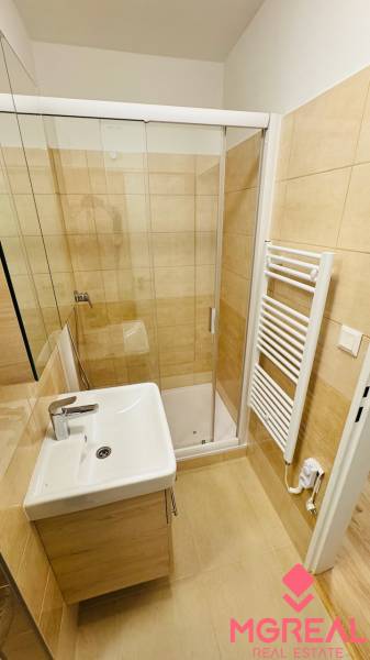 Fürdőszoba csempézett burkolattal, zuhanyzóval és mosdóval egy egyszobás lakásban.