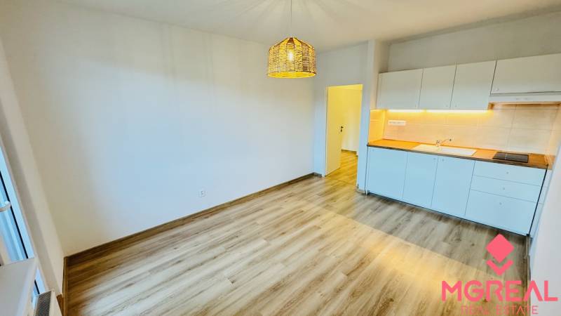 Konyha egy egyszobás lakásban fehér szekrényekkel és fa mintázatú padlóval.