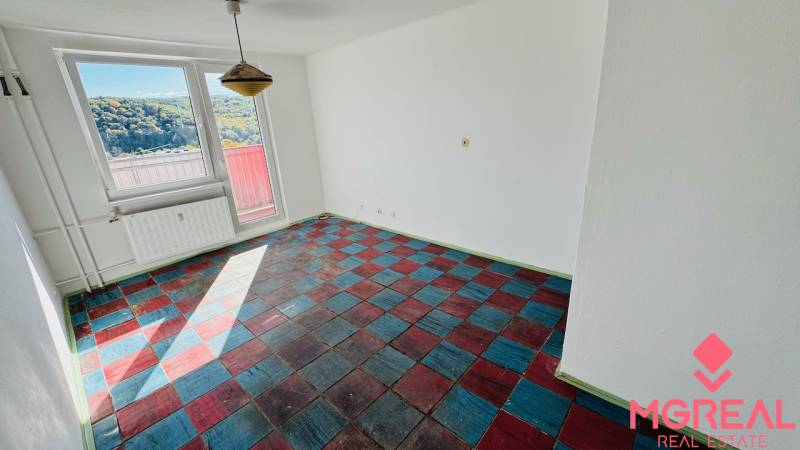 Szoba egy egyszobás lakásban színes padlóval és nagy ablakokkal, kilátással a természetre.