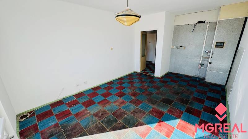 Szoba egy egyszobás lakásban színes csempézett padlóval és függő lámpával.