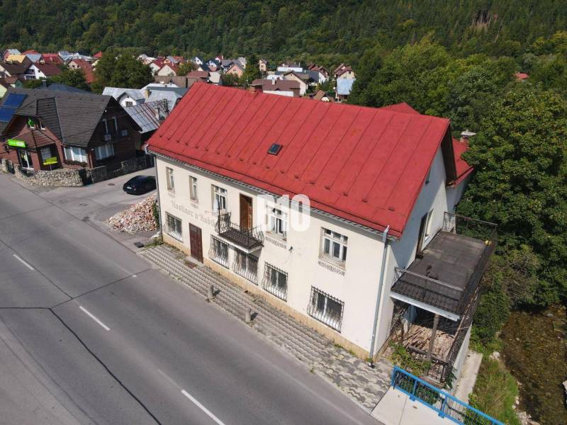 Az épület Bélán piros tetővel, környező házak és természet.