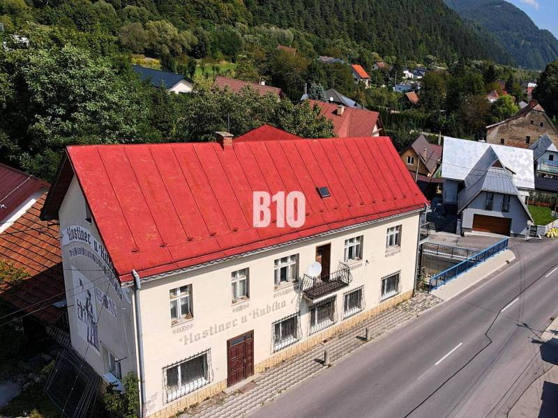 Egy piros tetős épület Bélán a főutcán, zölddel és házakkal körülvéve.