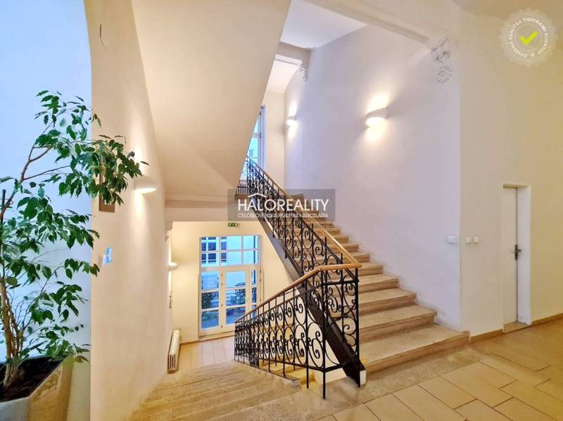 Világos lépcsőház díszes korláttal, amely irodákhoz vezet.