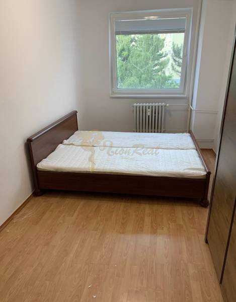 Hálószoba ággyal, radiátorral és fapadlóval egy kétszobás lakásban.