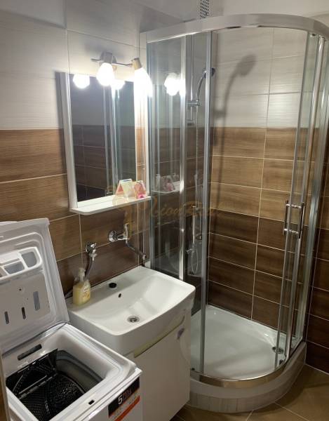 Fürdőszoba egy kétszobás lakásban mosdóval, zuhanyzóval és mosógéppel.