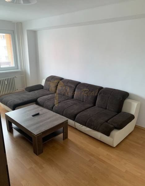 Nappali egy kétszobás lakásban sötét kanapéval és fa hatású padlóval.