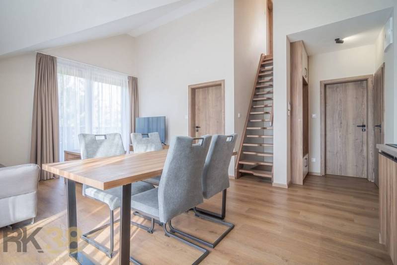 Nappali étkezőasztallal és lépcsővel egy kétszobás lakásban, fa dekoros padlóval.