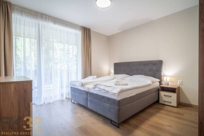 Hálószoba egy kétszobás lakásban világos függönyökkel és fa dekoros padlóval.