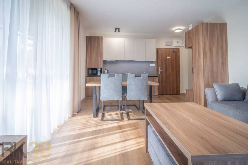 2 szobás lakás belső tere konyhasarokkal, szürke székekkel és fa mintázatú padlóval.