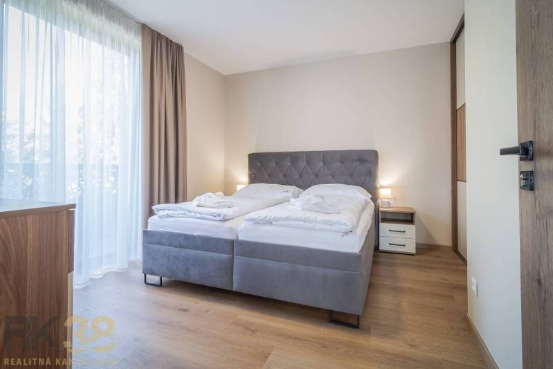 Hálószoba egy kétszobás lakásban kényelmes ággyal, fa dekorációjú padlóval és függönyökkel.