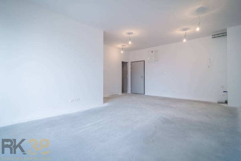 Tágas nappali egy kétszobás lakásban, fehér falak, alapvilágítás.