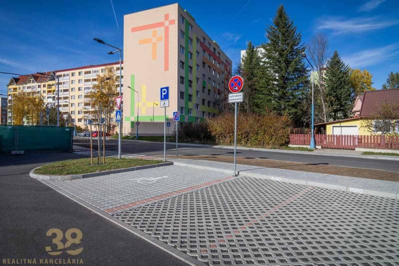 Lakóház és parkoló Poprádon, a háttérben zöld terület és házak.