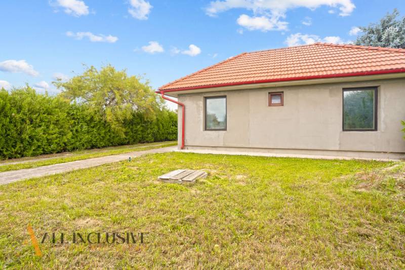 Családi ház Bátorkeszin piros tetővel, zöld gyep és bokrok veszik körül.