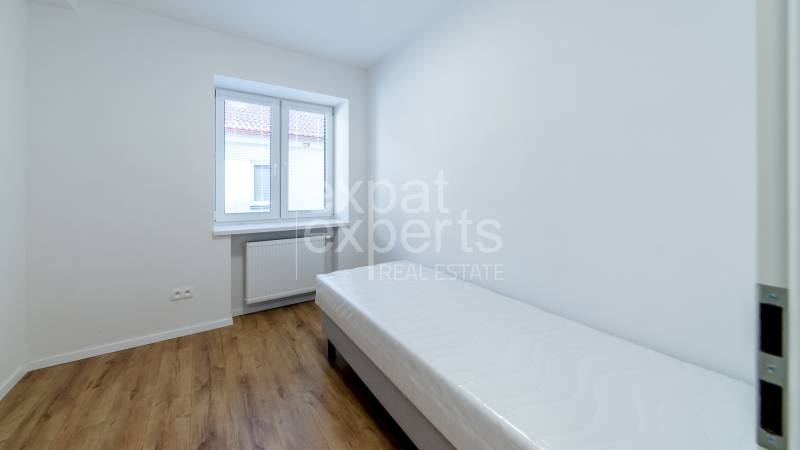 Szoba egyszemélyes ággyal, ablakkal és fa dekorációjú padlóval egy háromszobás lakásban.