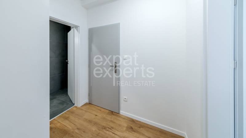 Folyosó szürke ajtókkal, sötét csempékkel rendelkező fürdőszobával és fa dekorációjú padlóval.