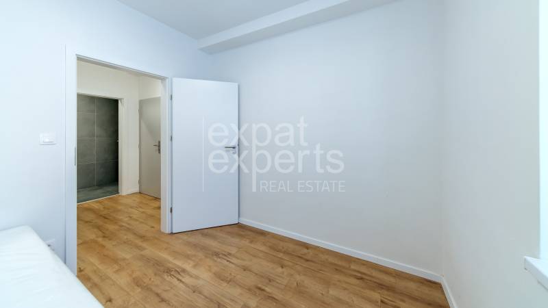 Szoba egy háromszobás lakásban fa dekorációjú padlóval és fehér falakkal.