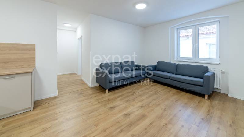 Nappali kék kanapéval és fa mintázatú padlóval egy háromszobás lakásban.