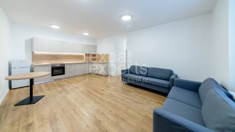 Konyha és nappali egy háromszobás lakásban, fa dekor padlóval, szürke kanapékkal és asztallal.