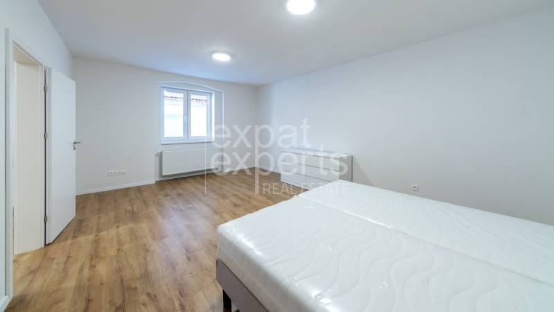 Világos hálószoba fa dekoros padlóval, ággyal és ablakkal egy háromszobás lakásban.