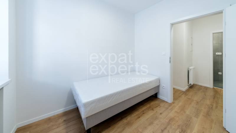 Egyszerű szoba egy háromszobás lakásban, ággyal és fa dekorációjú padlóval.