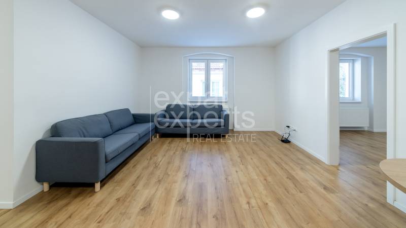 Nappali egy háromszobás lakásban kanapéval és fa dekorációjú padlóval.