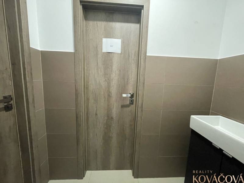 Kereskedelmi helyiségek belső tere WC ajtóval, burkolt falak, kerámia mosdó.