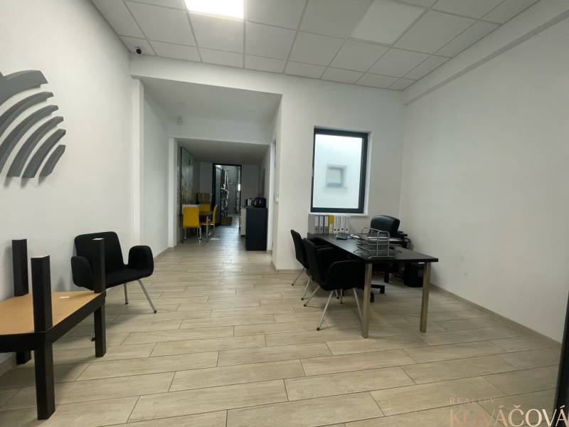 Kereskedelmi helyiségek fa mintázatú padlóval, minimalista bútorokkal és feltűnő székekkel.