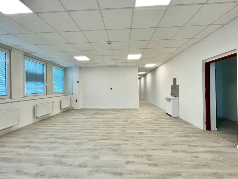 Irodák fa hatású padlóval, fehér falakkal és nagy ablakokkal.