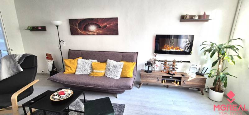 Nappali egy kétszobás lakásban kanapéval, polccal és elektromos kandallóval.