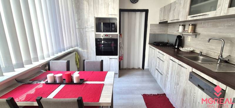 Konyha étkezőasztallal, fehér redőnyökkel és konyhabútorral egy kétszobás lakásban.