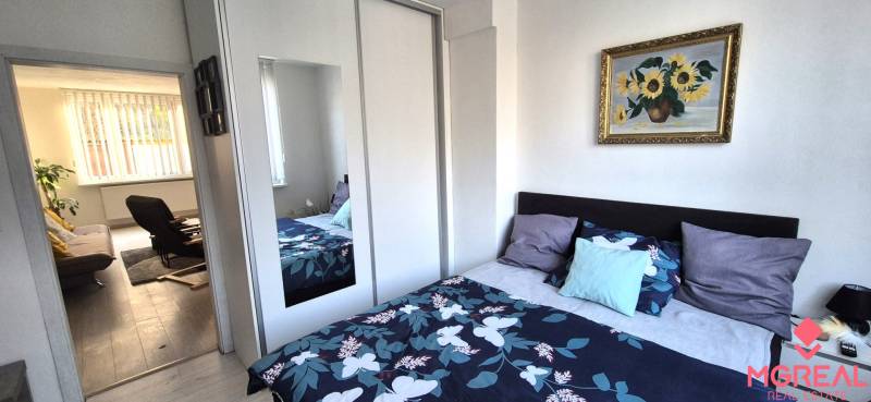 Hálószoba színes ággyal és szekrénnyel egy kétszobás lakásban, amely a nappaliba vezet.