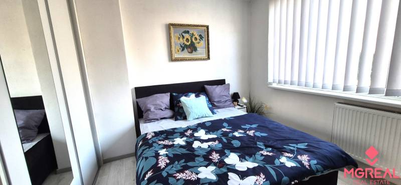 Hálószoba egy kétszobás lakásban ággyal, képpel és tükrös szekrénnyel.