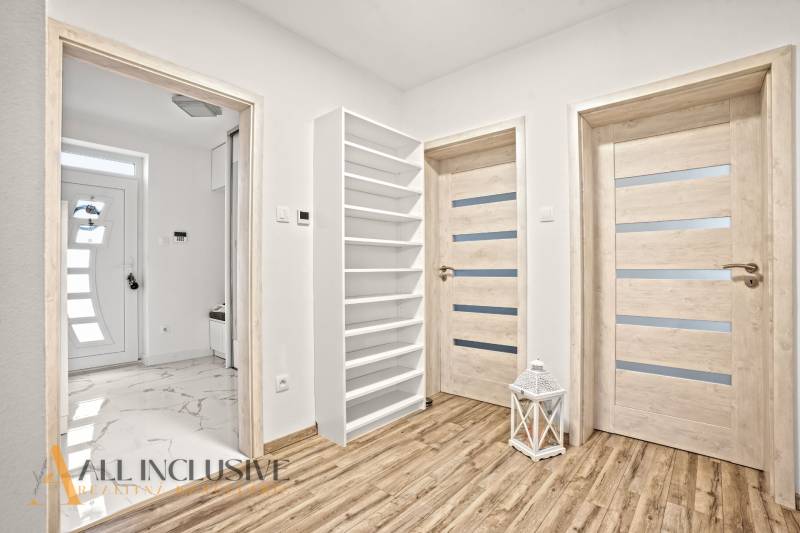 Családi ház belső tere fa dekorációjú padlóval, ajtókkal és fehér polccal.