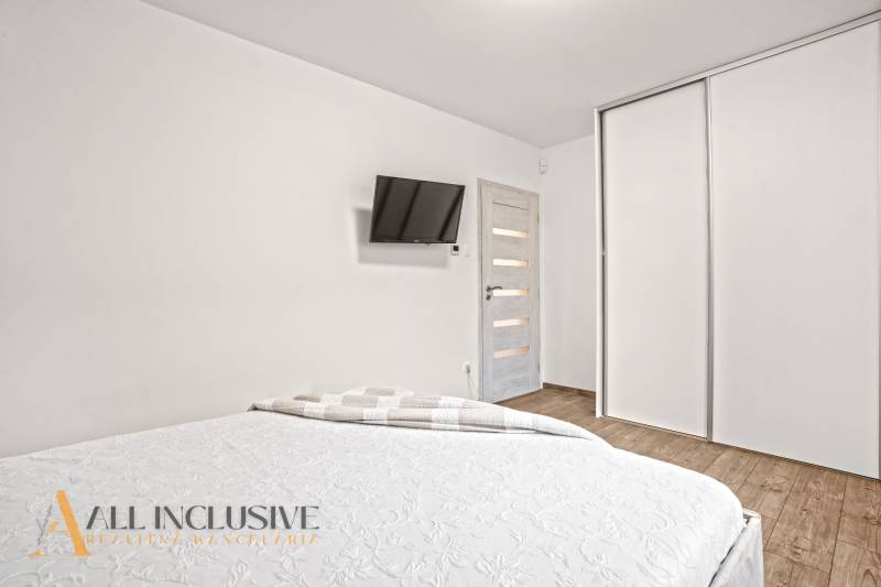 Hálószoba családi házban fehér szekrényekkel, falra szerelt TV-vel és fa dekorációjú padlóval.