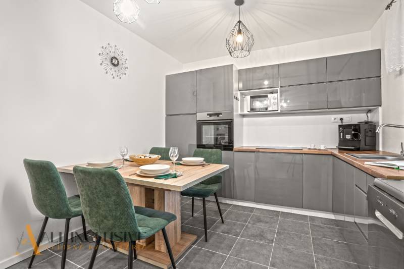 Konyha egy családi házban szürke konyhabútorral, étkezőasztallal és zöld székekkel.