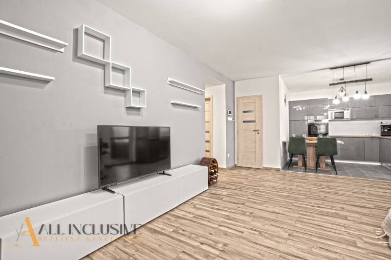 Nappali egy családi házban fa dekoros padlóval, televízióval, étkezőasztallal és konyhával.