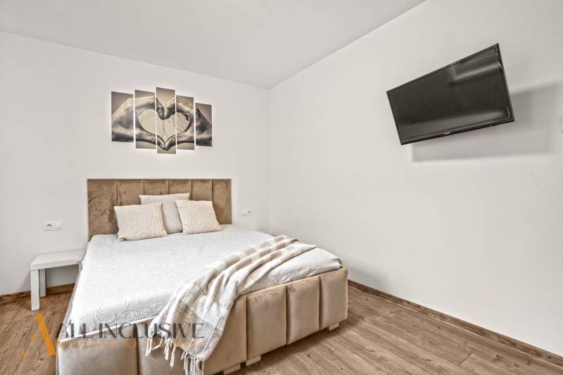 Hálószoba családi házban kényelmes ággyal, televízióval és fa dekoros padlóval.