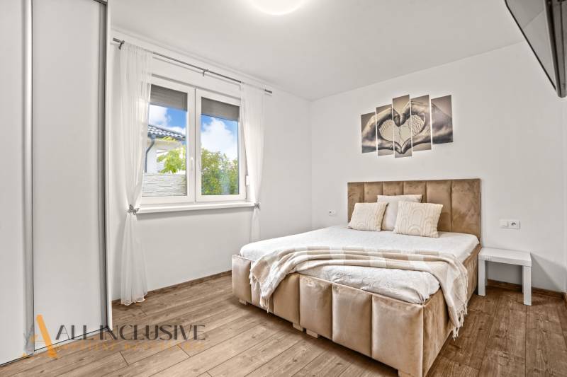 Hálószoba világos ágykerettel, fa hatású padlóval és fali képpel egy családi házban.