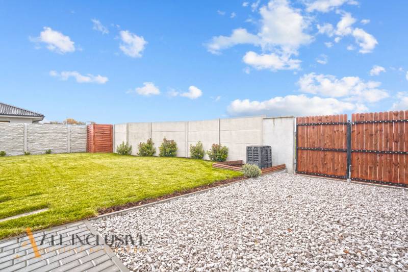 Kert a családi ház mellett Gabčíkovo-ban, gyep, kavicsok és fa kerítés.