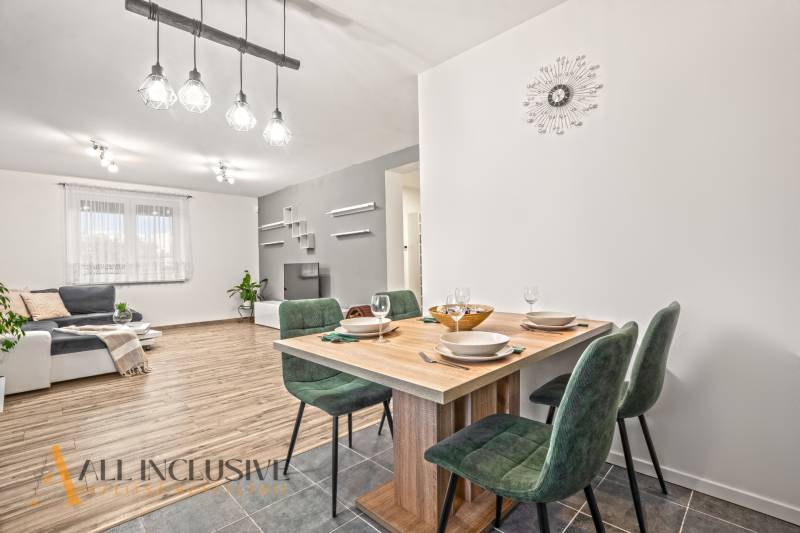 Családi ház belső tere fa dekorációjú padlóval, étkezőasztal és zöld székek.