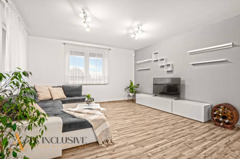 Nappali egy családi házban kanapéval, televízióval és fa dekorációjú padlóval.