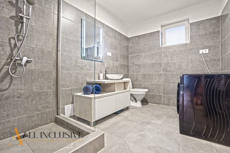 Fürdőszoba családi házban csempékkel, zuhanyzóval, mosógéppel és mosdóval.