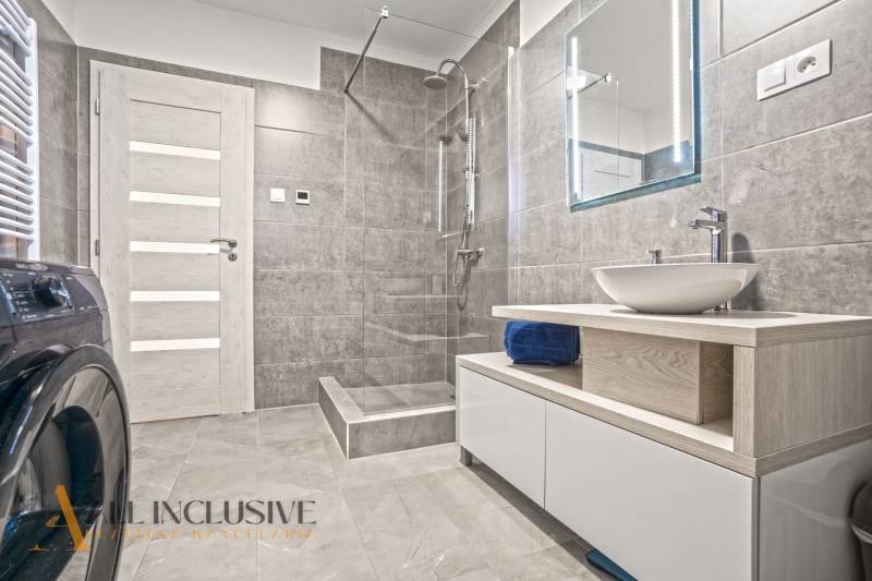 Fürdőszoba zuhanyzóval, fa deszkán lévő mosdóval és mosógéppel a családi házban.