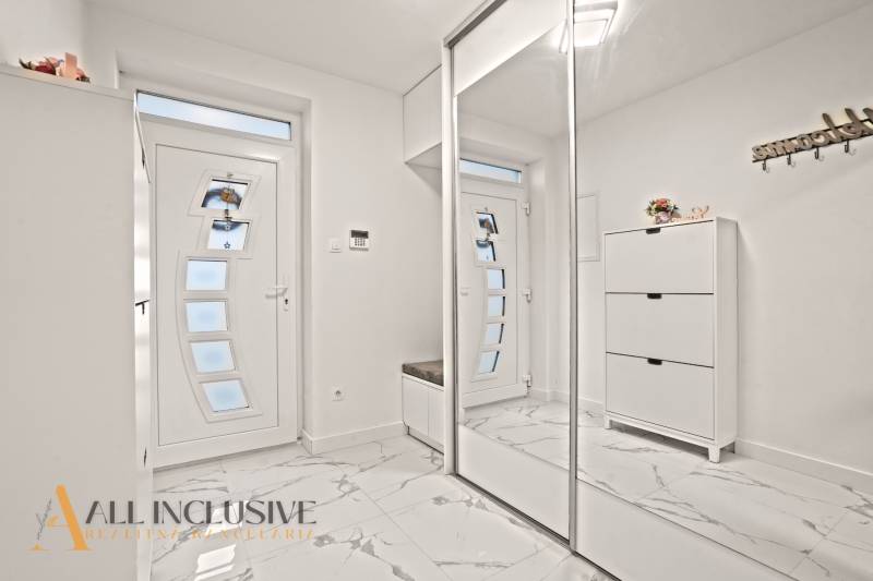 Családi ház belső tere fehér szekrényekkel, tükörrel és márvány mintás padlóval.