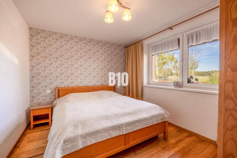 Hálószoba családi házban virágos tapétával és fa dekoros padlóval.